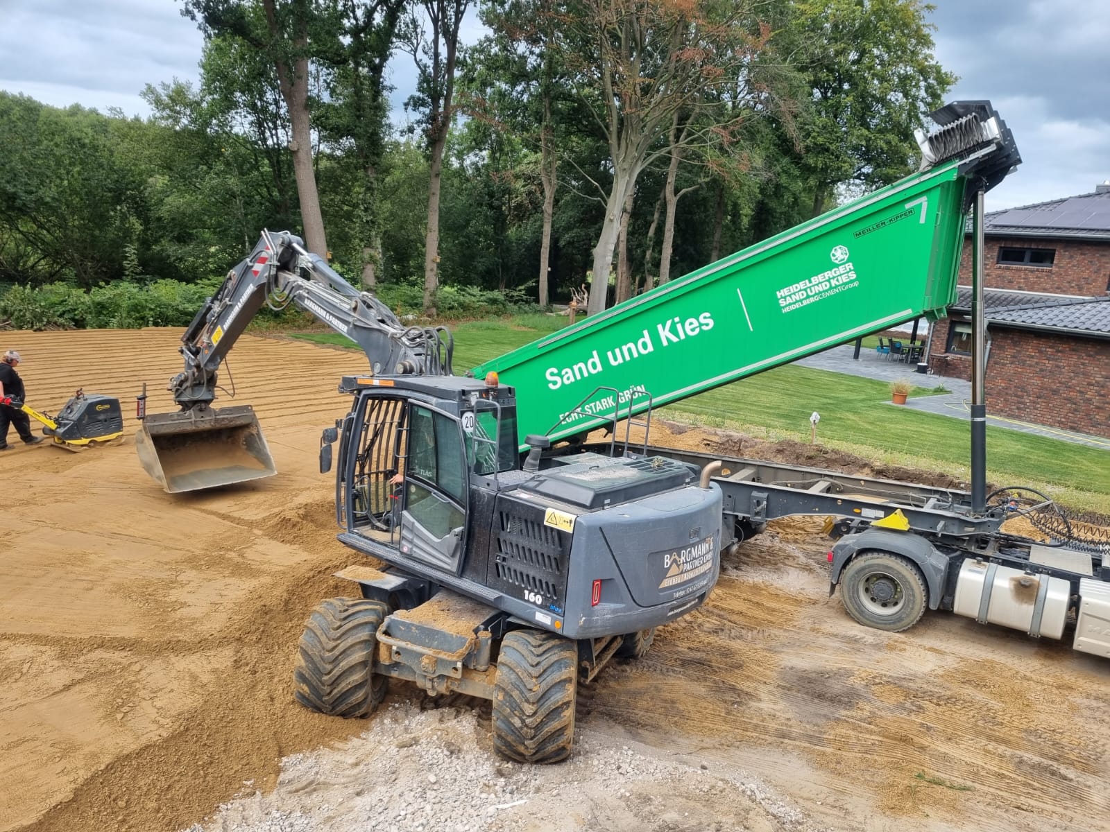 Bagger und Transportanhänger auf einer sandigen Baufläche